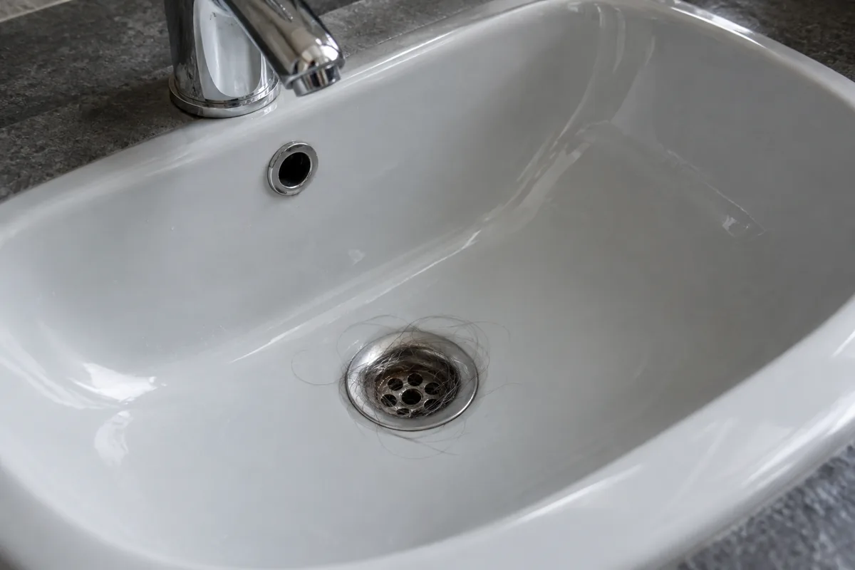 Quelques cheveux sont retenus autour d’une bonde de lavabo ouverte.