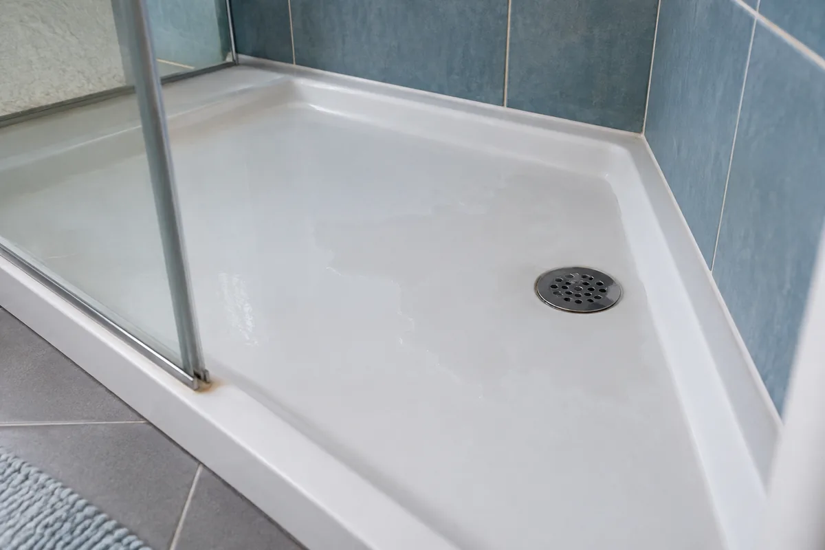 Petit fond d’eau autour de la bonde d’un receveur de douche blanc.