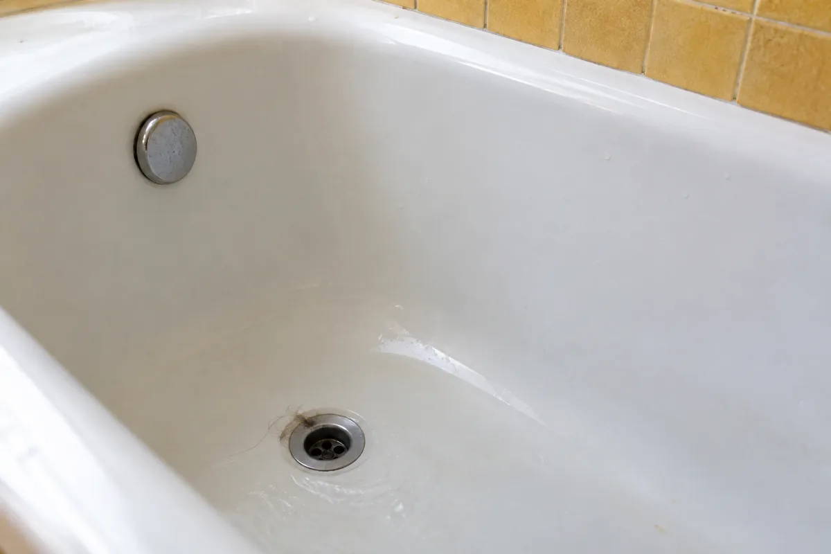 Quelques cheveux au bord de la bonde ouverte d’une baignoire.