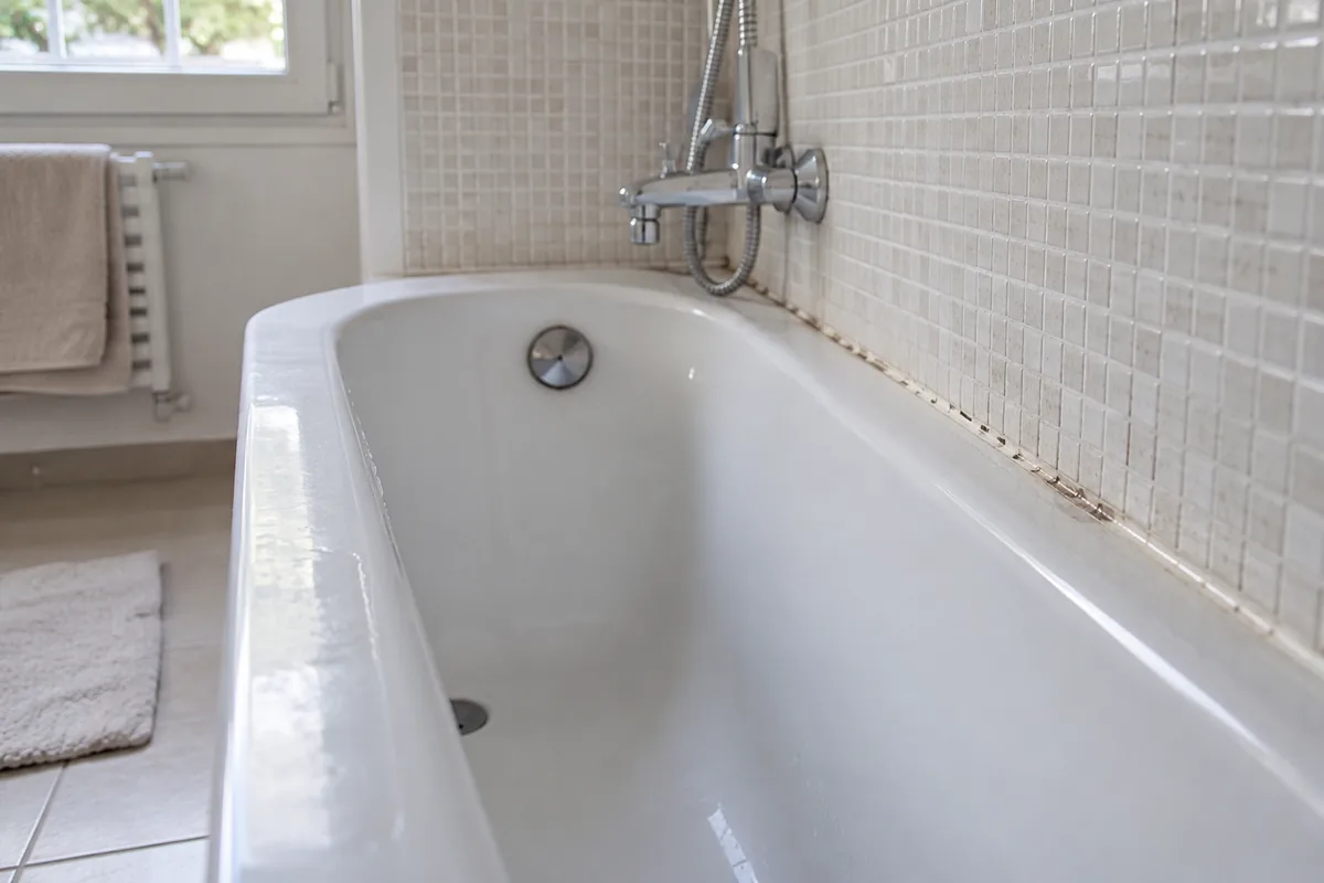 Trace humide localisée sur le bord d’une baignoire carrelée.